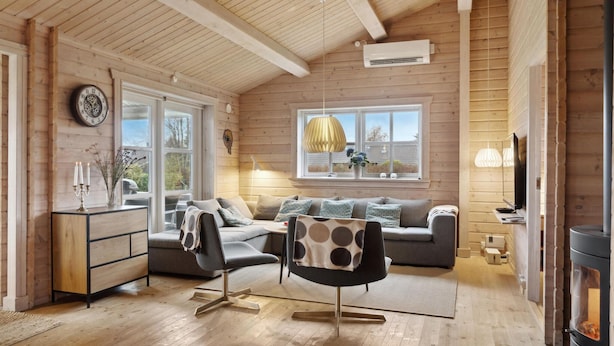 Ein gemütliches Blockhaus-Interieur mit Holzbalkendecke, einer Couch, einem Sessel, einem Schreibtisch und einem Kamin.