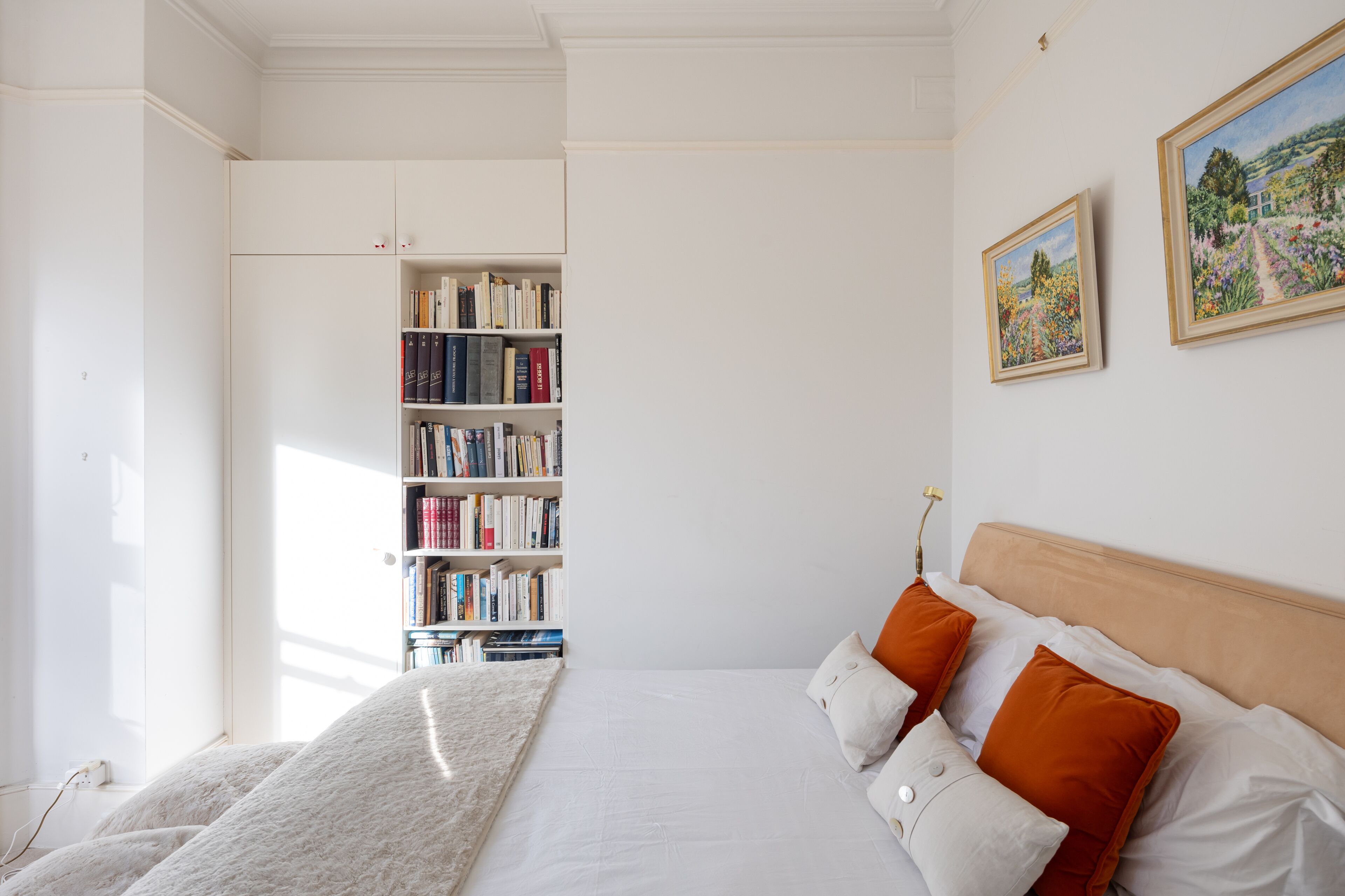 Un dormitorio con una cama grande, una estantería y dos cuadros en la pared.