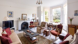 A spacious living room with a fireplace, comfortable seating, and large windows offering a view of the outdoors. - Courtside Charms, by Veeve (London)