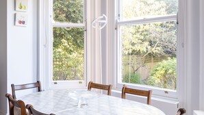 A dining area with a round table, six wooden chairs, and large windows with white frames. - Courtside Charms, by Veeve (London)