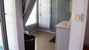 A bathroom with a white sink, a towel rack, a shower with a white towel, and a black basket.