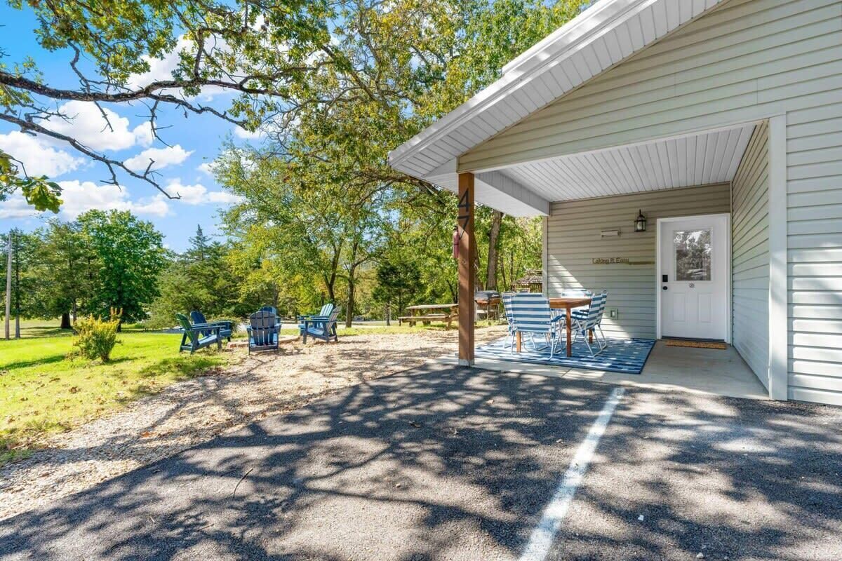 A covered outdoor seating area with tables and chairs, a gravel path, and a building with a door labeled "Lakeside B Cottage".