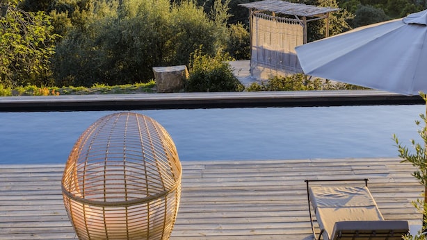 A wooden deck with a pool, a wicker chair, and a lounge chair overlooking a mountainous landscape. - Terre de Maquis (Sari-d'Orcino)