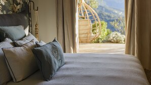A bed with pillows and a view of a mountainous landscape through a window. - Terre de Maquis (Sari-d'Orcino)