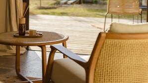 A room with a view of a hill and a building, a wicker chair, a small round table, and a bottle of reed sticks. - Terre de Maquis (Sari-d'Orcino)