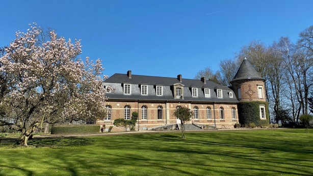 A large, historic building with a central tower and symmetrical windows, surrounded by a well-maintained lawn and flowering trees. - Le Domaine Saint Ange (Friville-Escarbotin)