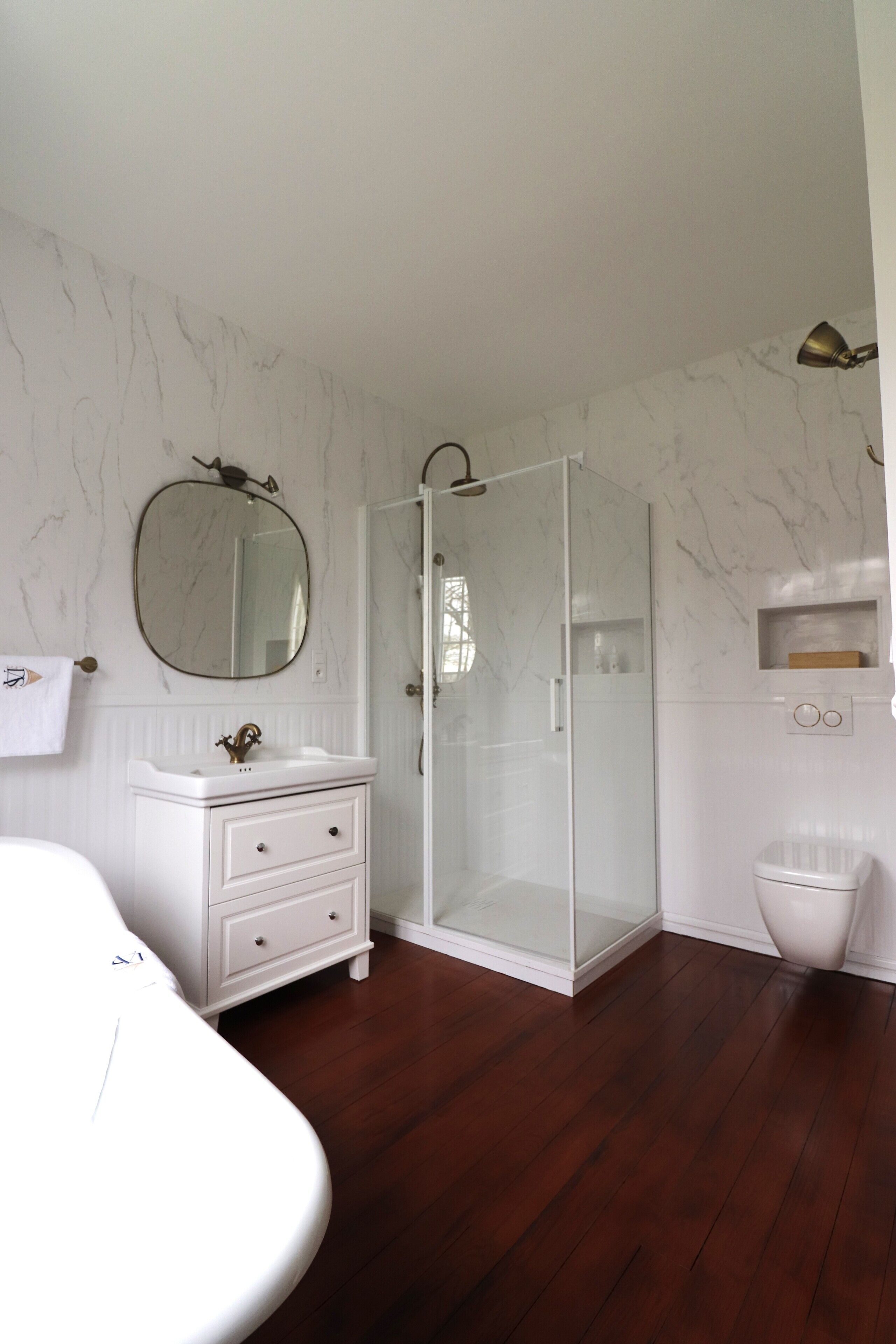 A bathroom with a white vanity, a glass shower enclosure, and a marble-patterned wall.