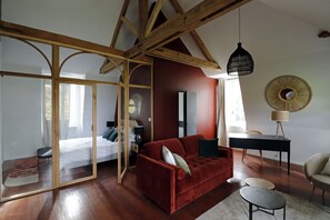 A modern room with a red sofa, a desk, and a mirror. There is a bed with a wooden headboard and a window. - Le Domaine Saint Ange (Friville-Escarbotin)