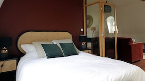 A bedroom with a wooden ceiling, a bed with white bedding, a red chair, and a small table with a lamp. - Le Domaine Saint Ange (Friville-Escarbotin)