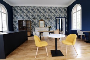 A room with a wooden floor, a white round table, and two yellow chairs. There is a fireplace with a mirror above it, and a bookshelf to the left. - Le Domaine Saint Ange (Friville-Escarbotin)