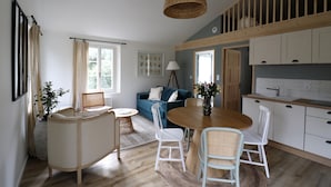 A cozy, well-lit room with a dining table, chairs, a sofa, and a kitchen area. - Le Domaine Saint Ange (Friville-Escarbotin)