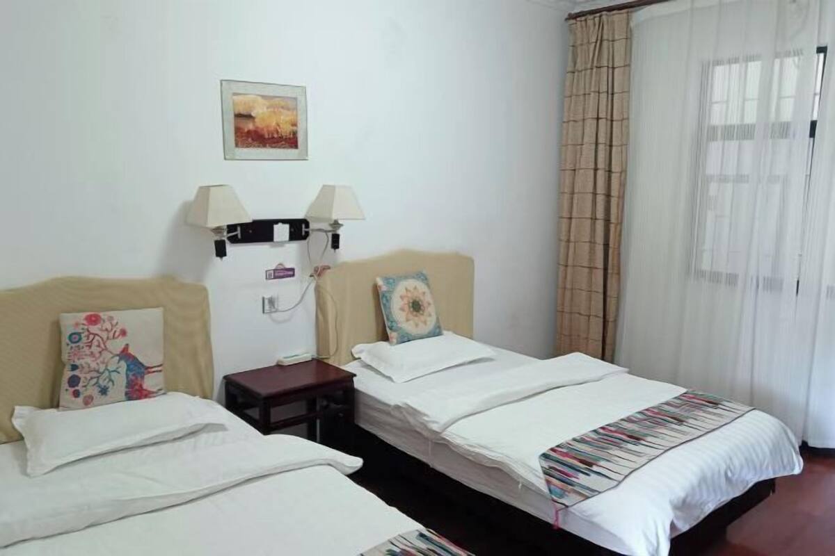 A hotel room with two single beds, a small table, a lamp, and a painting on the wall.