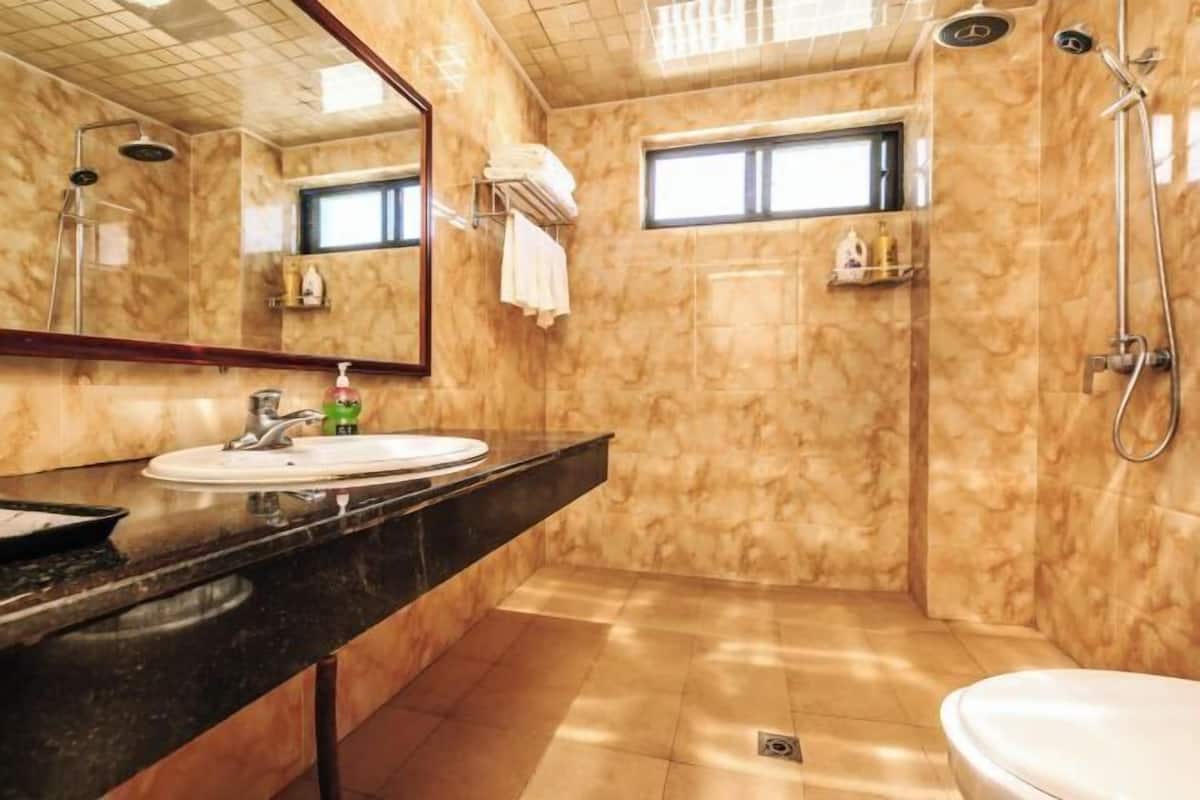 A bathroom with a marble wall, a sink, a mirror, a shower, and a toilet.