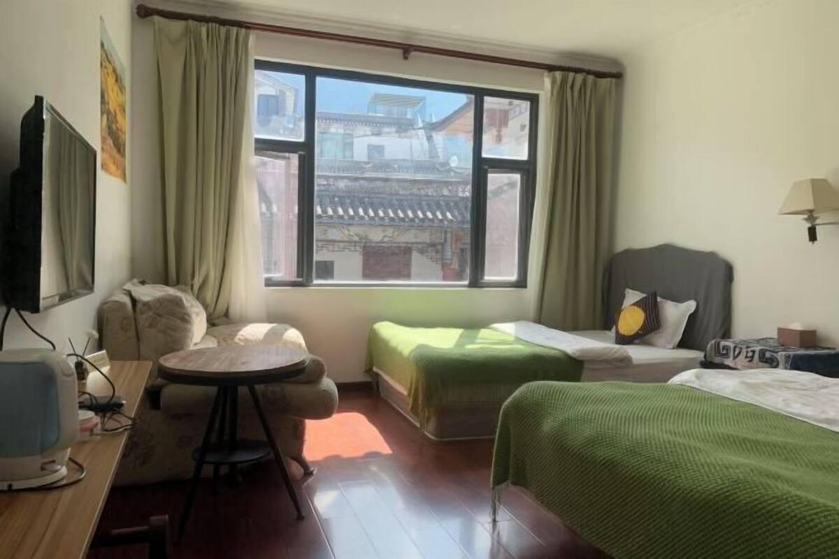 A hotel room with a bed, a desk with a computer, a chair, and a window with curtains.