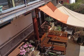 Un espace extérieur abrité, aménagé avec des tables et des chaises, entouré de plantes en pot et d’un vélo.
