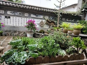 A courtyard with a variety of potted plants and a stone wall with inscriptions.