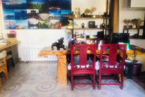 Un coin repas avec une table en bois et des chaises rouges, un radiateur et un mur orné de tableaux encadrés.