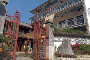 Un bâtiment traditionnel avec une porte rouge, un chemin de pierre et un balcon agrémenté de balustrades.