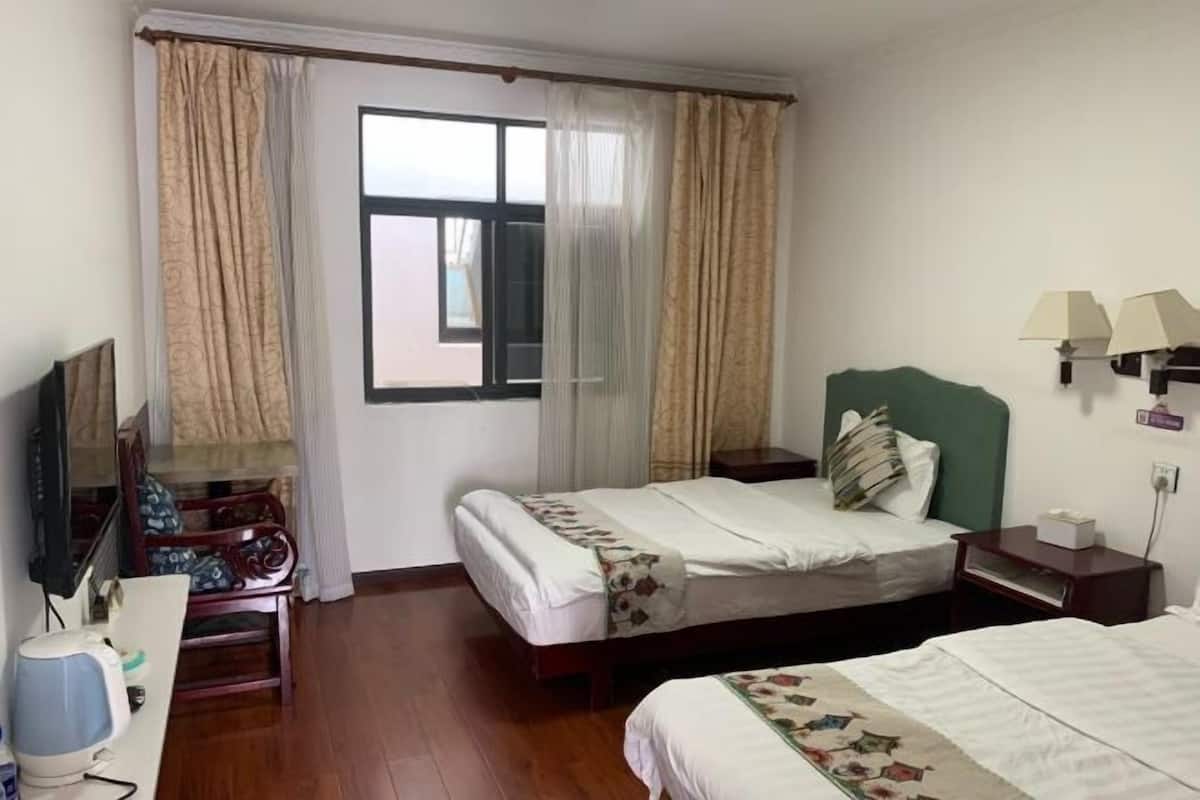 A hotel room with two beds, a television, a desk with a lamp, and a window with curtains.
