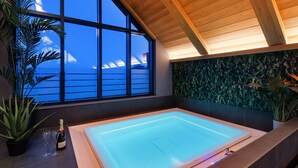 A modern indoor swimming pool with a view of the ocean through large windows, surrounded by tropical plants and a wooden ceiling. - Stylish Northumberland retreat in the heart of Amble (Amble)
