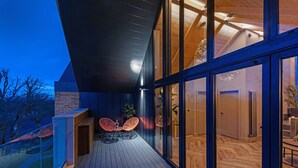 A modern outdoor patio with a wooden deck, glass doors, and a seating area with two chairs. - Stylish Northumberland retreat in the heart of Amble (Amble)