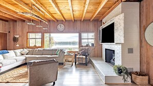 Una sala de estar acogedora, con techo de madera, chimenea, sofá y televisor montado en la pared.
