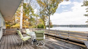 Una terraza de madera con mobiliario exterior, con vista a un lago.