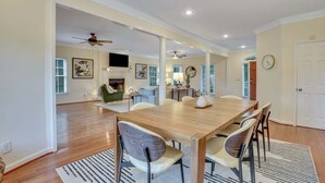 A spacious dining area with a wooden table and chairs, a ceiling fan, and a view into the living room.