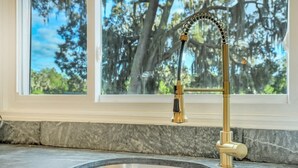 A kitchen sink with a gold faucet and a window above it.