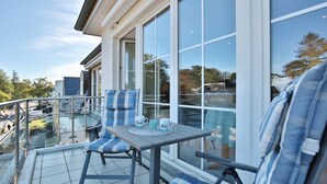A balcony with a glass railing, a table, and two chairs with striped cushions. - Haus Schäfer Appartement 8 (Timmendorfer Strand)