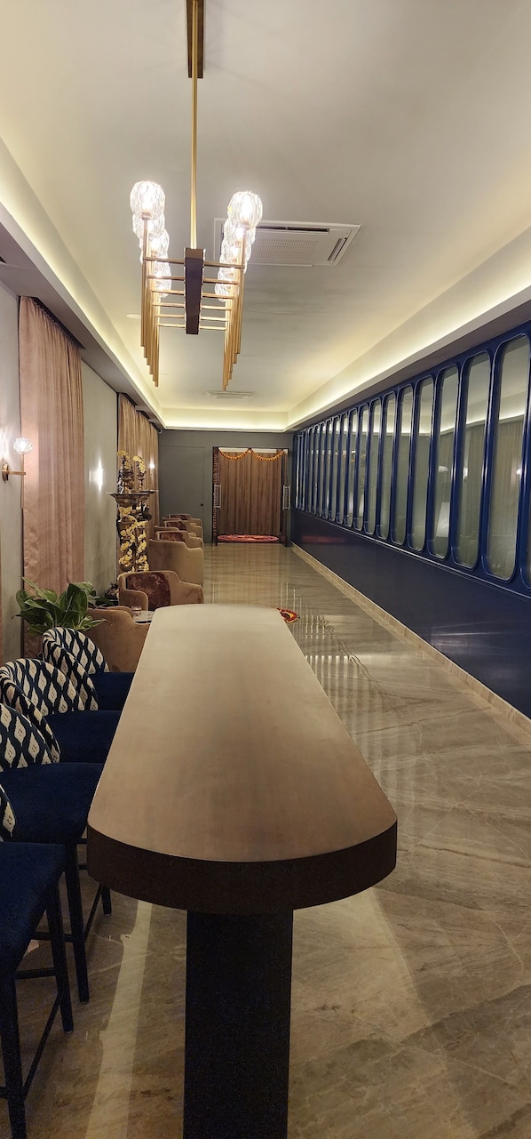 A modern hotel lobby with a long reception desk, comfortable seating, a chandelier, and a view of the hallway.