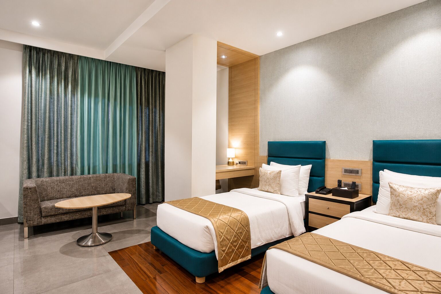 A hotel room with two beds, a sofa, a small table, and a desk with a lamp.