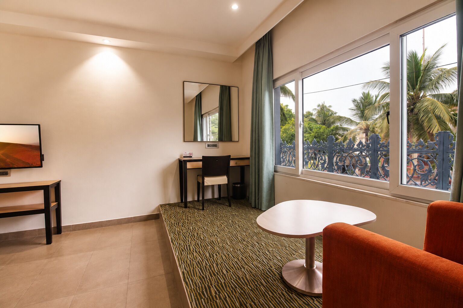 A hotel room with a desk, chair, round table, and a large window with a view of palm trees.