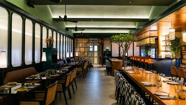 Un restaurante con mesas largas, sillas y una zona de bar.
