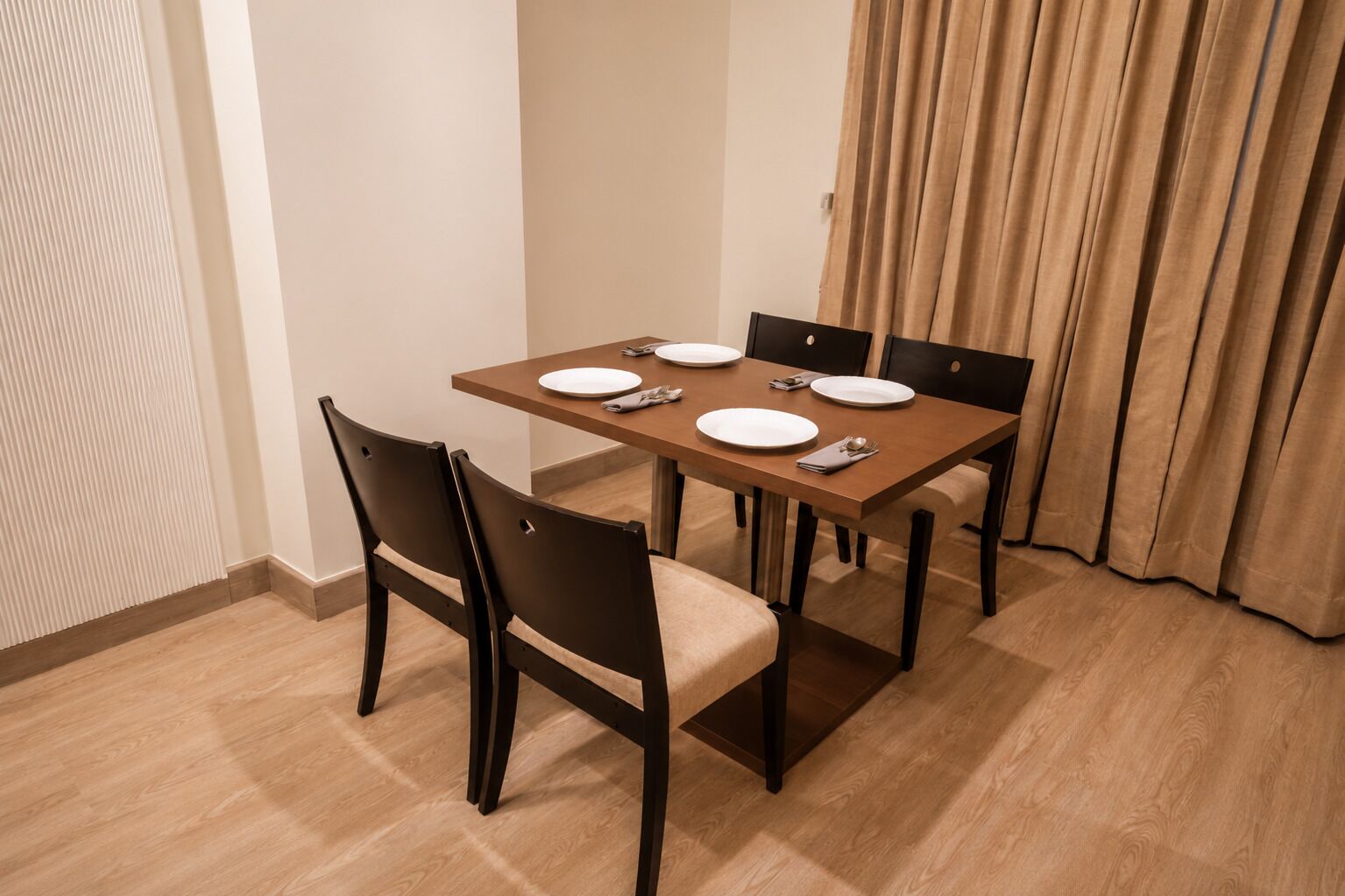 Un coin repas avec une table rectangulaire dressée pour quatre personnes, quatre chaises et une fenêtre avec des rideaux.