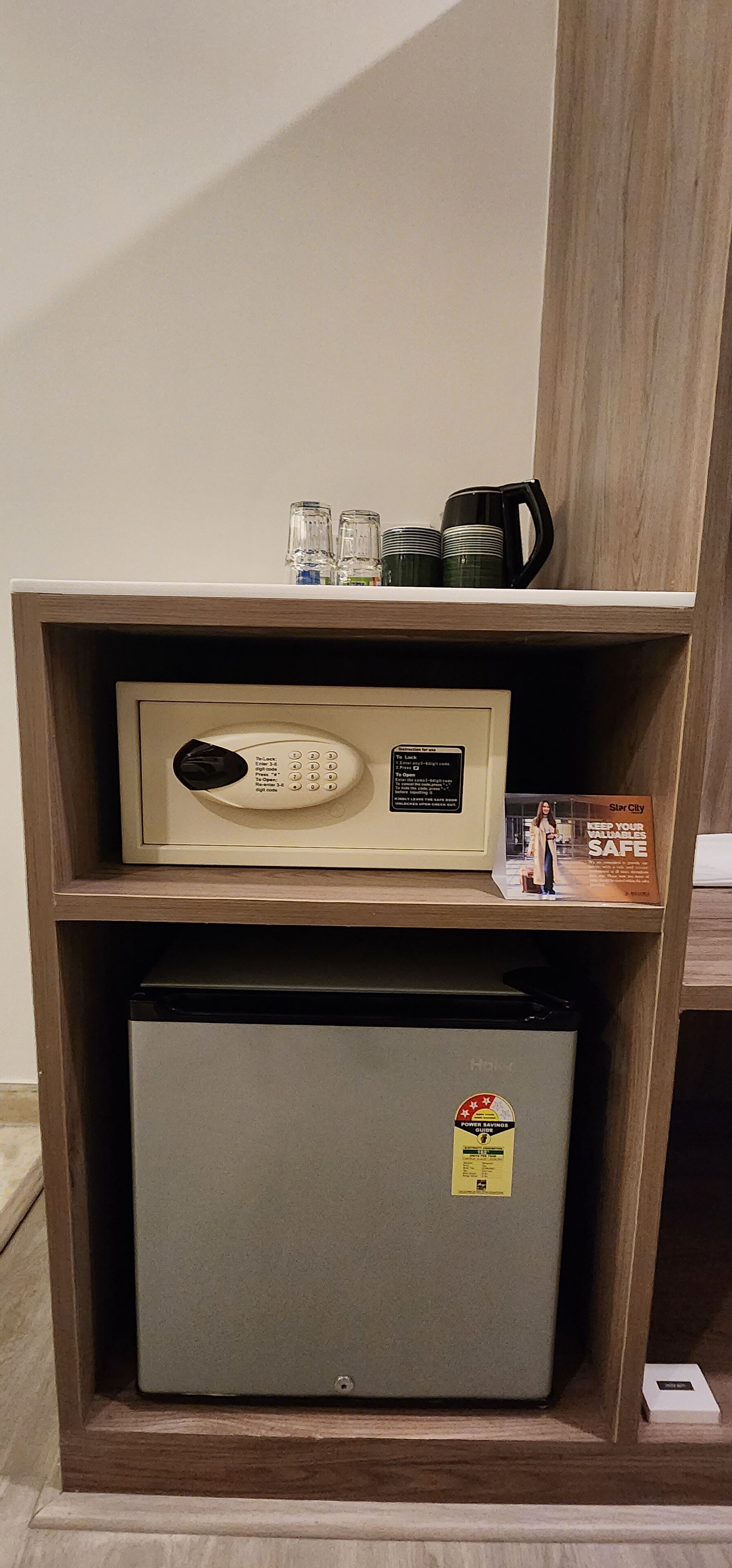 A compact refrigerator with a control panel and a sticker, placed on a wooden shelf with a glass door.