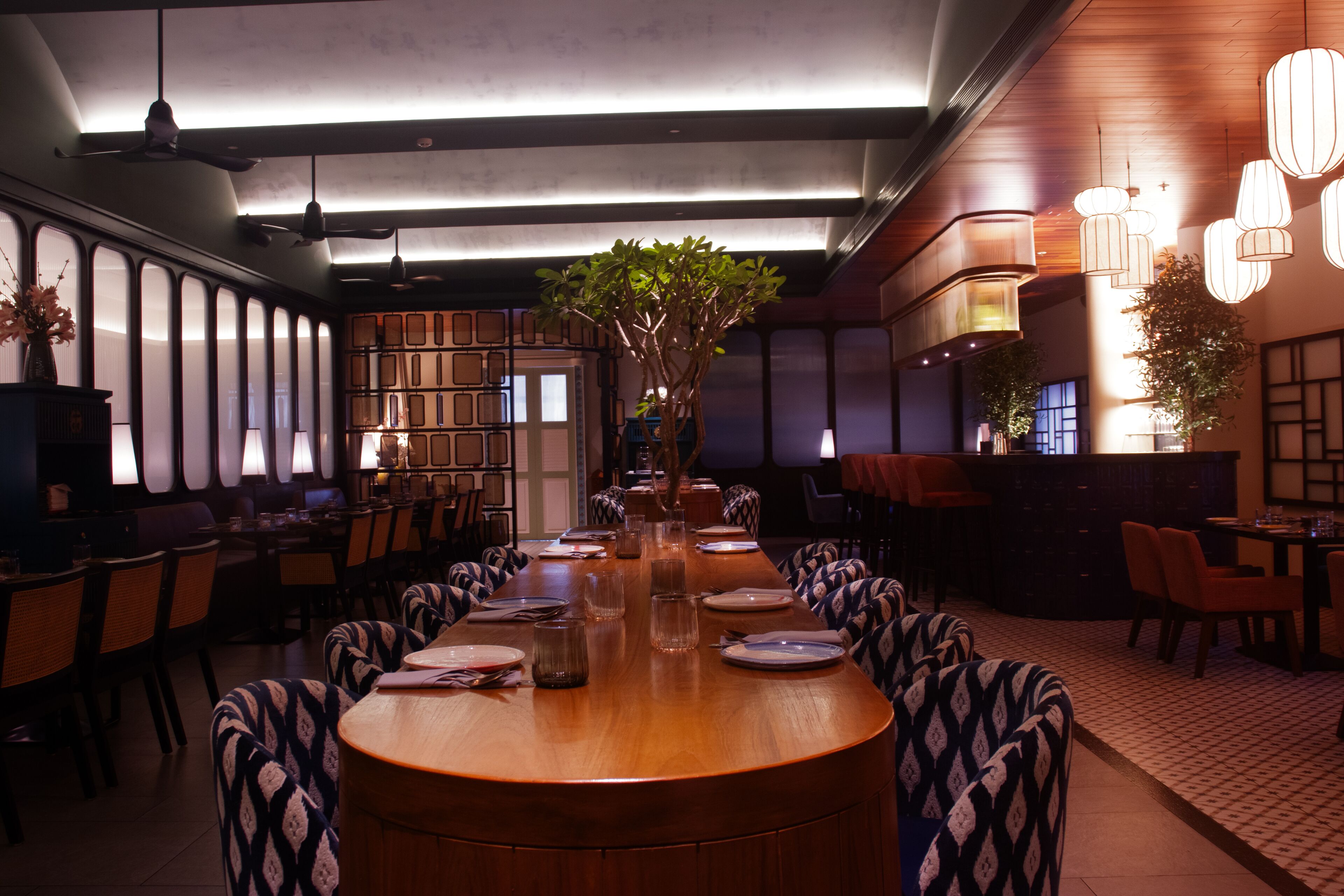 Un restaurant avec une longue table en bois, des chaises et des lampes suspendues.