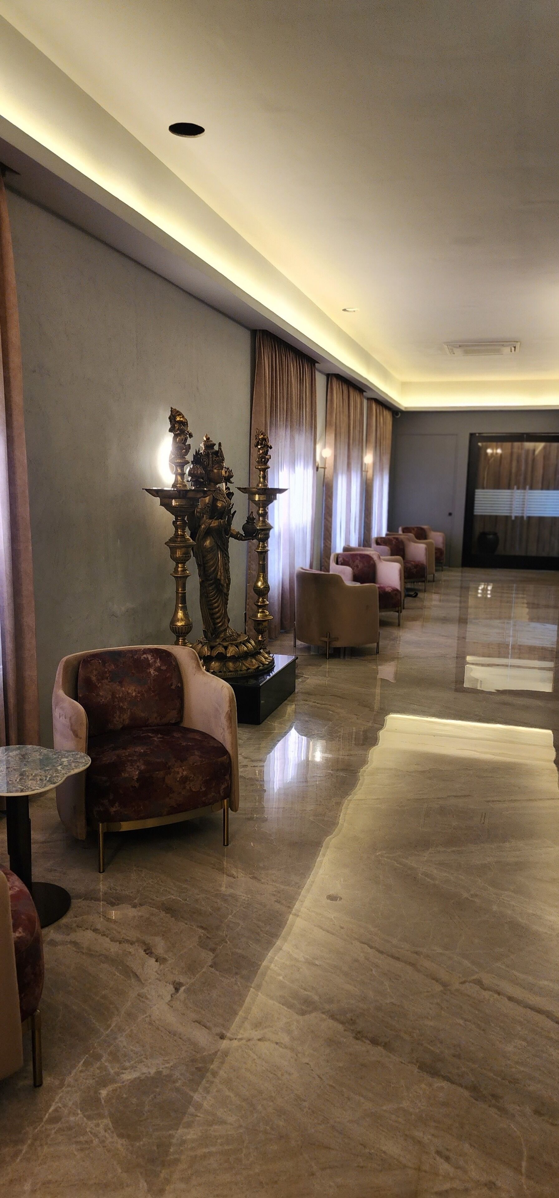 Un'elegante hall d'hotel moderna, con pavimento in marmo, comodi posti a sedere e statue decorative.