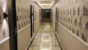 Un largo pasillo bien iluminado con papel tapiz estampado y suelo de mármol, que conduce a varias puertas.