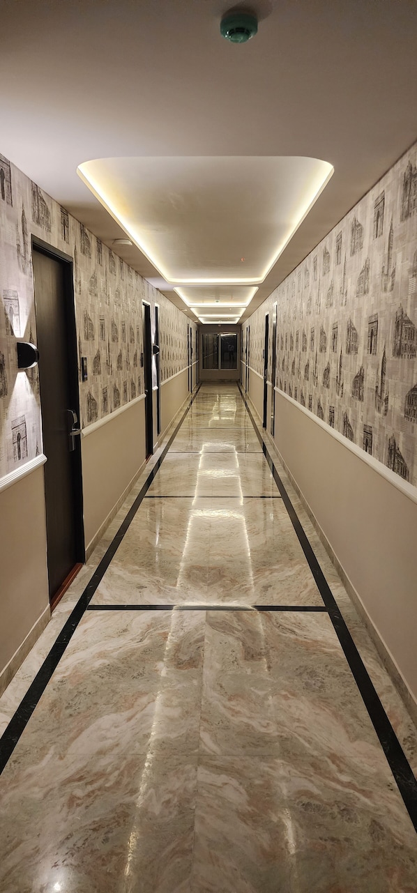 A long, well-lit hallway with patterned wallpaper and a marble floor, leading to multiple doors.