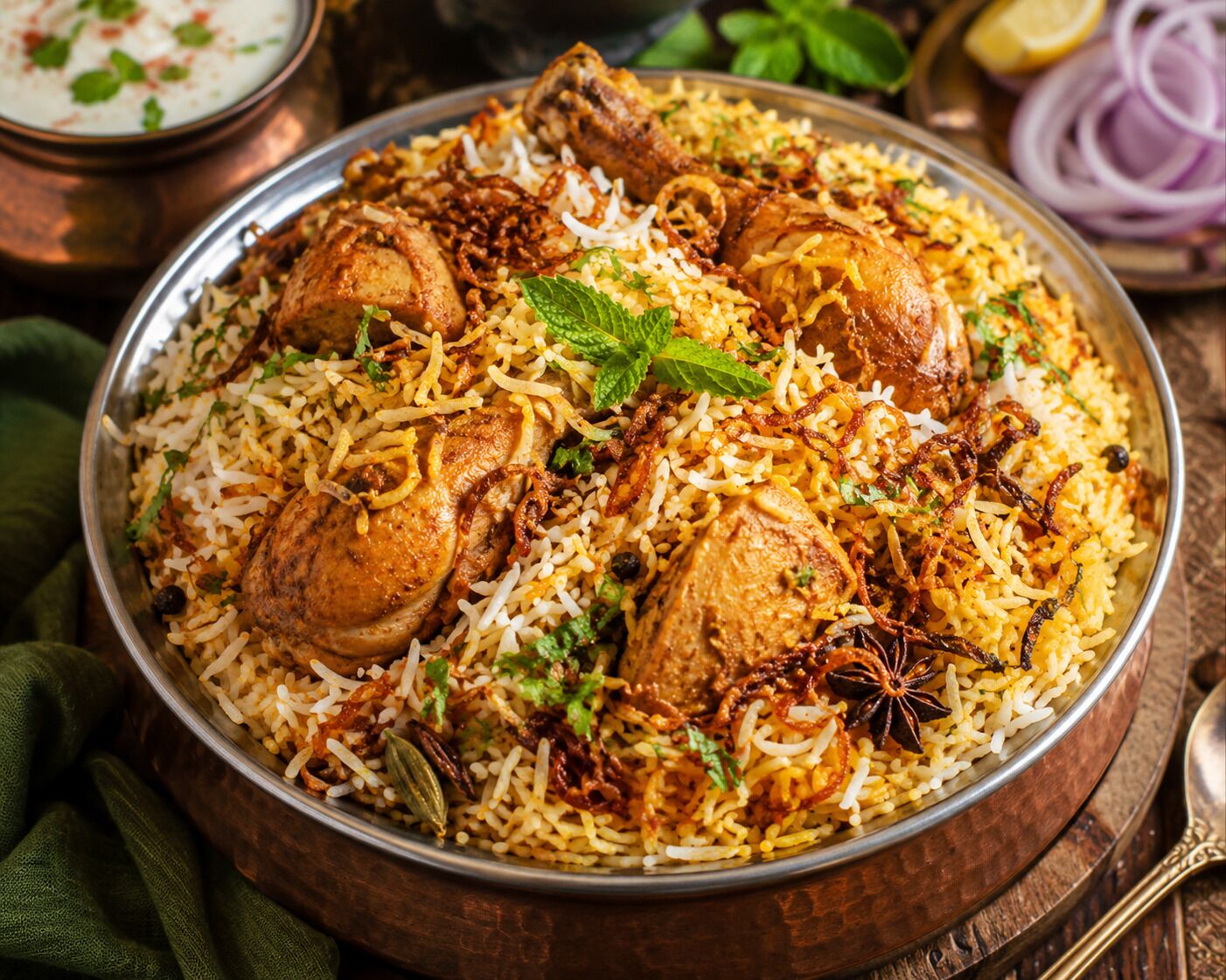 A large metal platter filled with biryani, garnished with herbs and fried onions.