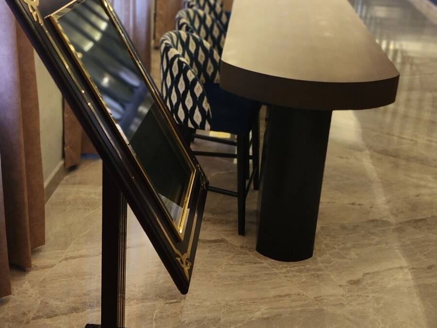 Un moderno vestíbulo de hotel con piso de mármol, un espejo con marco dorado y negro, una mesa de comedor y una silla estampada.