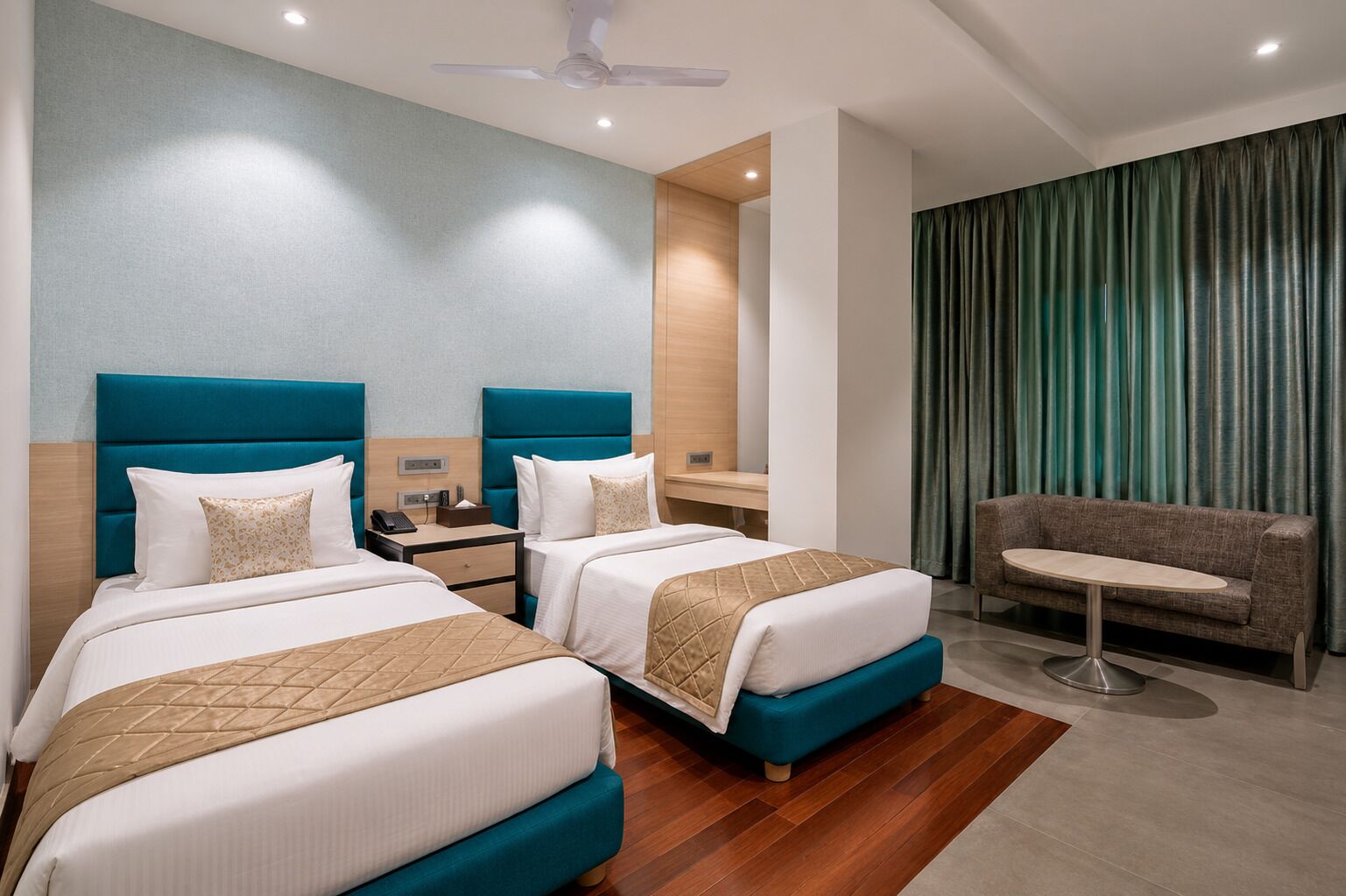 A hotel room with two beds, a sofa, a desk, and a ceiling fan.
