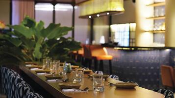 Un restaurante con una barra larga, asientos con cojines estampados y una planta grande.
