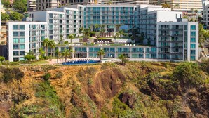 A modern hotel with multiple floors, a swimming pool, and a view of the surrounding landscape. - Madeira Palace Ocean Sounds (Funchal)