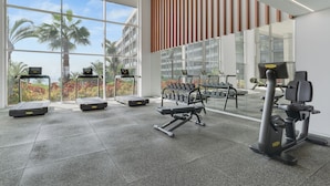 A modern gym with treadmills, dumbbells, and weight machines, large windows with a view of palm trees and buildings. - Madeira Palace Ocean Sounds (Funchal)