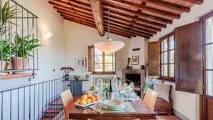 A dining area with a wooden table set for a meal, surrounded by chairs. A staircase with a railing is visible to the left. - Villa Debby in Lucca (Lucca)