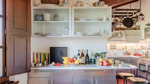 A modern kitchen with stainless steel cabinets, a central island with fruit, and hanging pots. - Villa Debby in Lucca (Lucca)