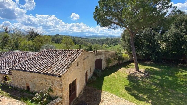 Un edificio rustico in pietra con tetto in tegole, un piccolo arco d'ingresso e un vialetto lastricato che vi conduce.