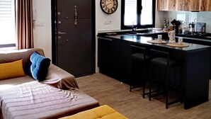 A modern apartment with a large bed, a yellow ottoman, a kitchen with a bar, and a large window. - Charme de L'atypique (Nabeul‎)